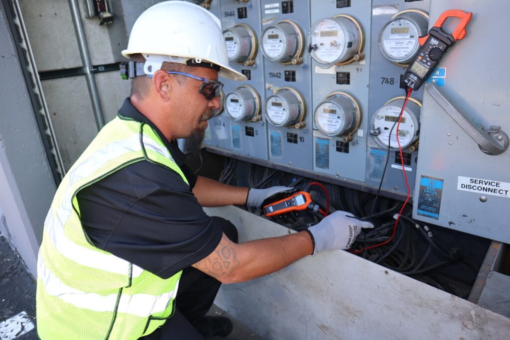 IMG2692 Clark Electric LV LLC Clark Electric LV LLC Licensed electrician in safety gear using a clamp meter to test electrical panel and meters