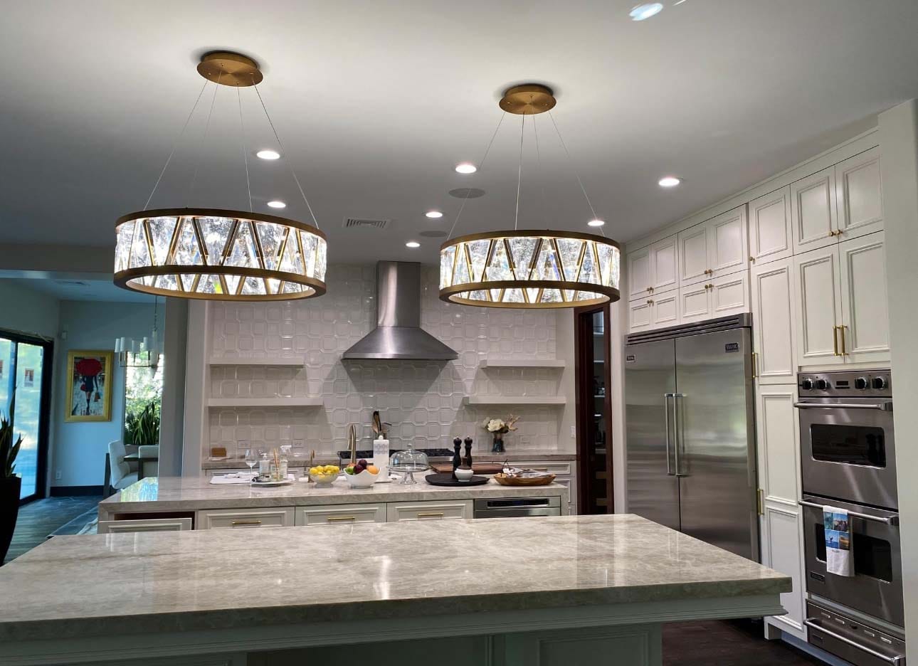 Modern kitchen featuring two pendant light fixtures suspended above an island with marble countertop and stainless steel appliances