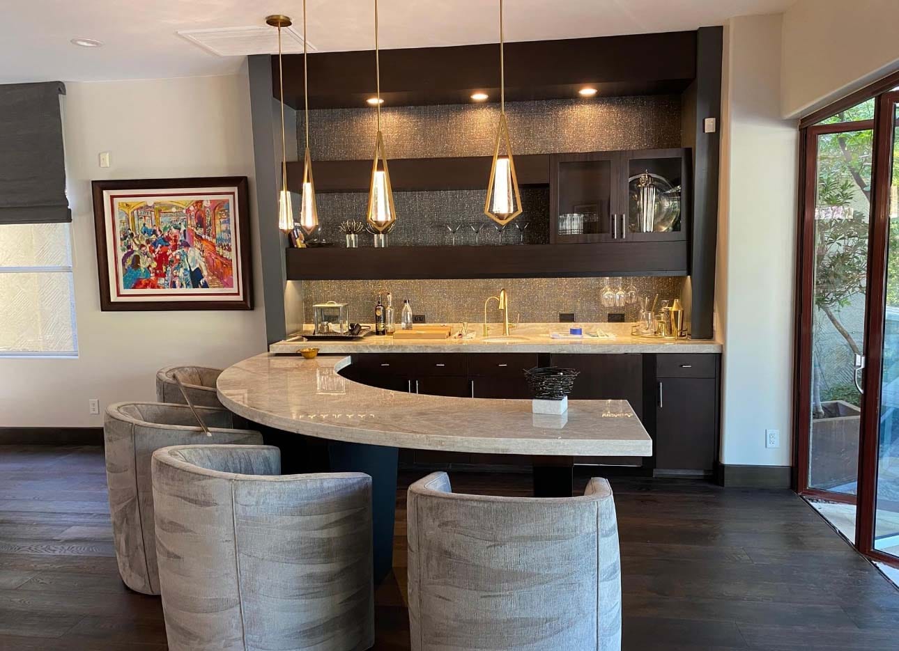 Modern home bar with pendant lighting dark cabinetry and curved marble countertop with upholstered seating