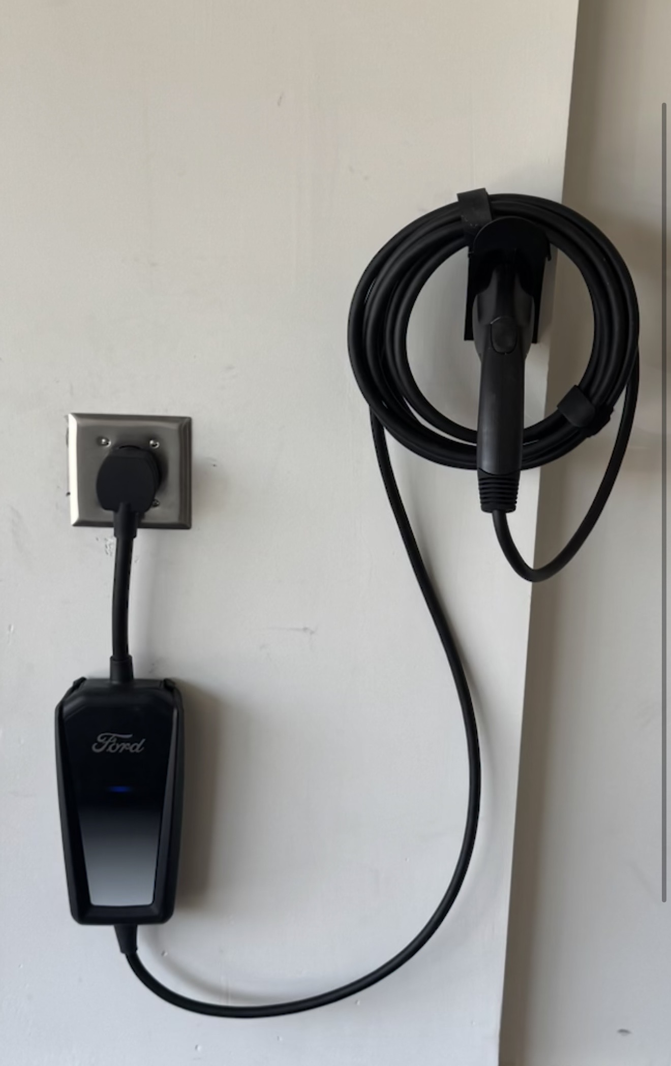 Ford electric vehicle charger mounted on a wall with a coiled charging cable and plug ready to use