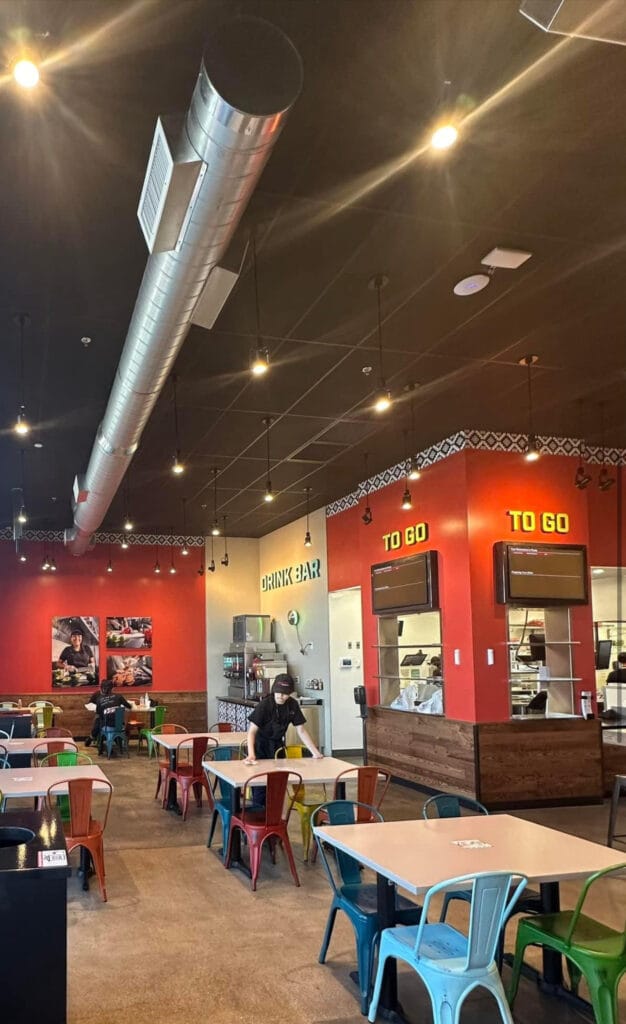 Modern restaurant interior with colorful metal chairs tables bright LED ceiling lights and red accent walls with a large metallic cylindrical duct feature