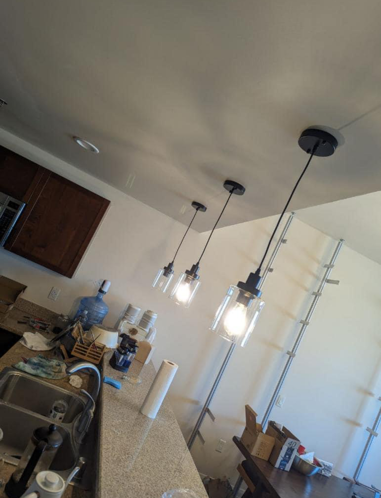 Kitchen island with three pendant lights above cluttered countertop water cooler and boxes in the background