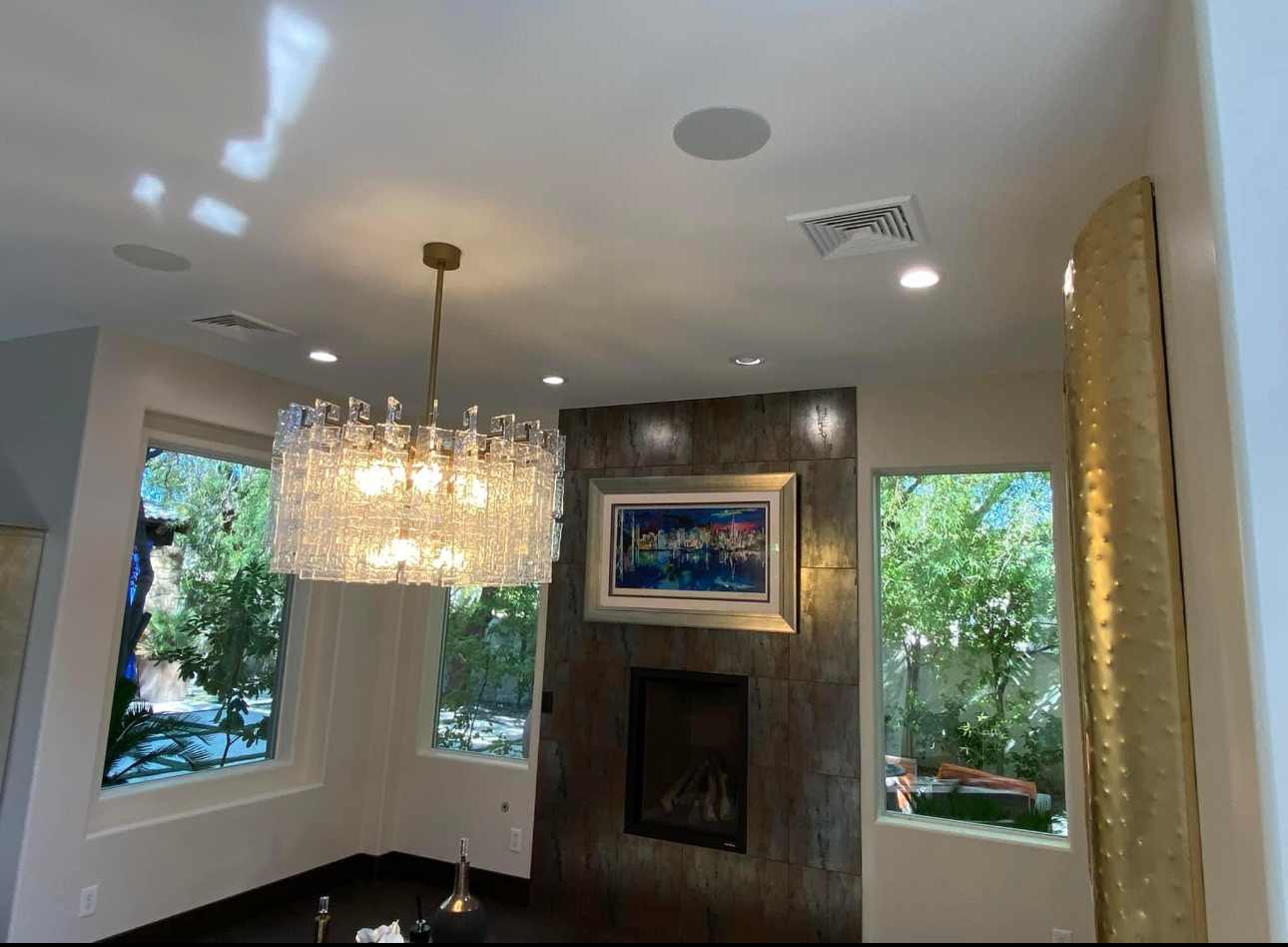 Modern living room with a glass chandelier hanging above a dark wood coffee table and a tile fireplace centerpiece with a framed painting above it