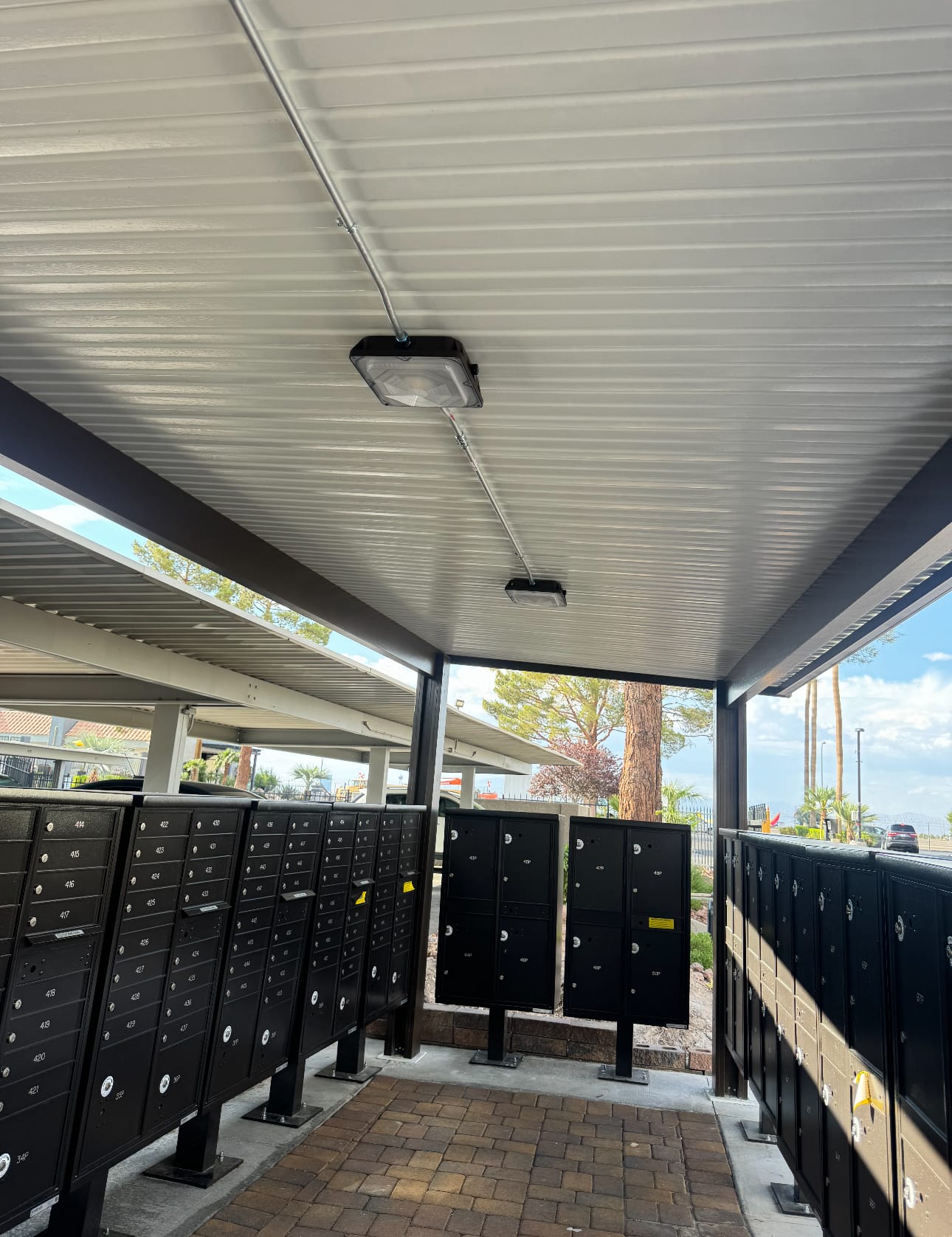 Modern covered mailroom with black mailboxes under a metal corrugated ceiling with LED lighting fixtures
