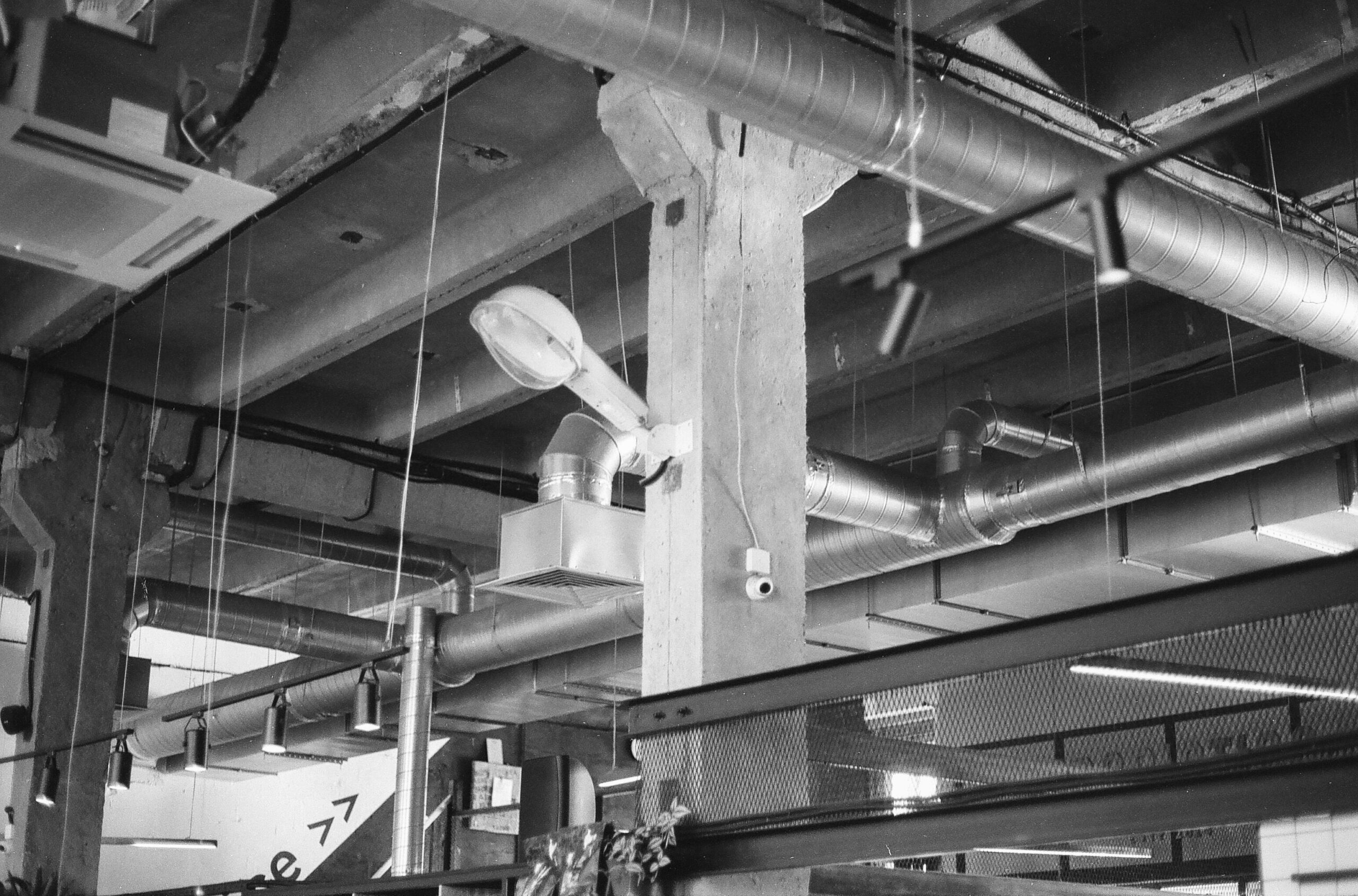 Industrial basement ceiling with exposed metal ducts pipes and a concrete support column hanging light fixtures visible along the ceiling