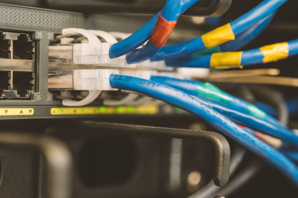 Close up of blue red and yellow Ethernet cables plugged into a patch panel in a server rack showing port connections labeled nearby