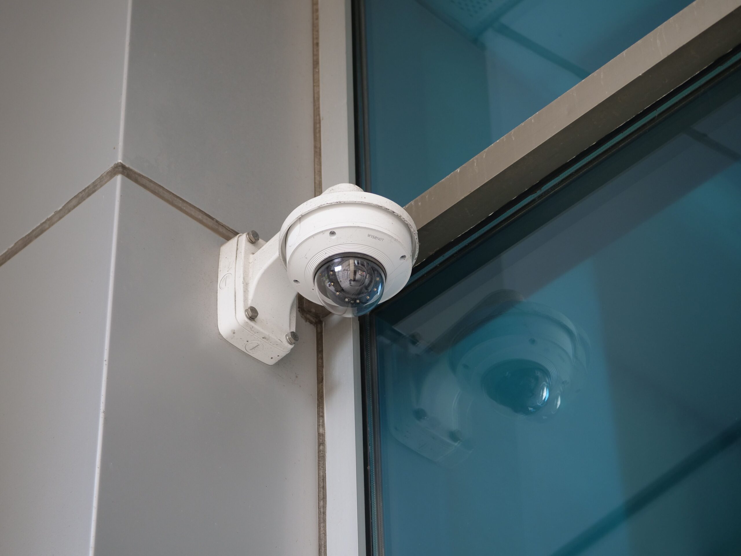 White dome security camera mounted on a bracket beside a glass storefront window monitoring the exterior entrance