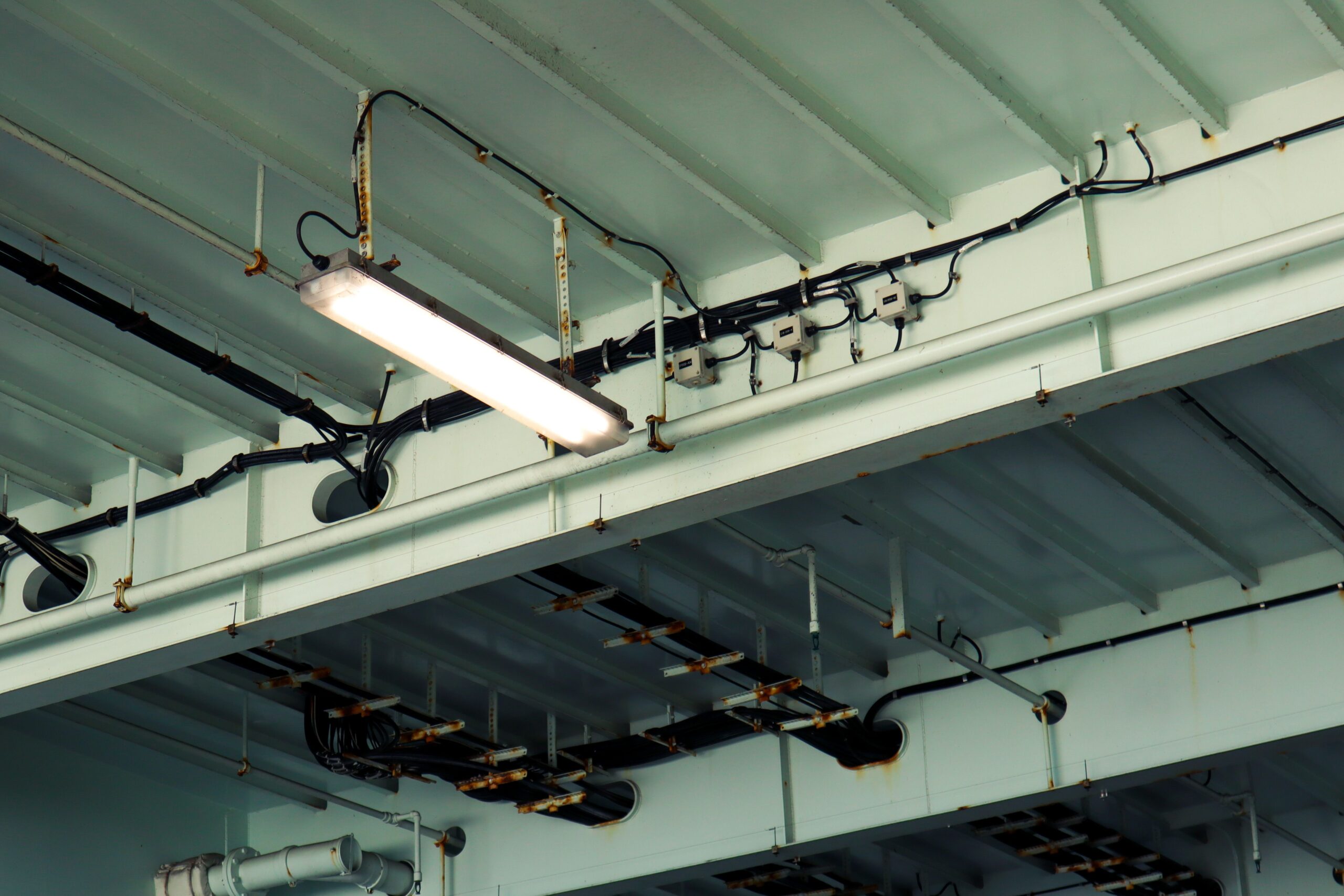 Industrial ceiling with exposed electrical conduits cables and a bright fluorescent light fixture
