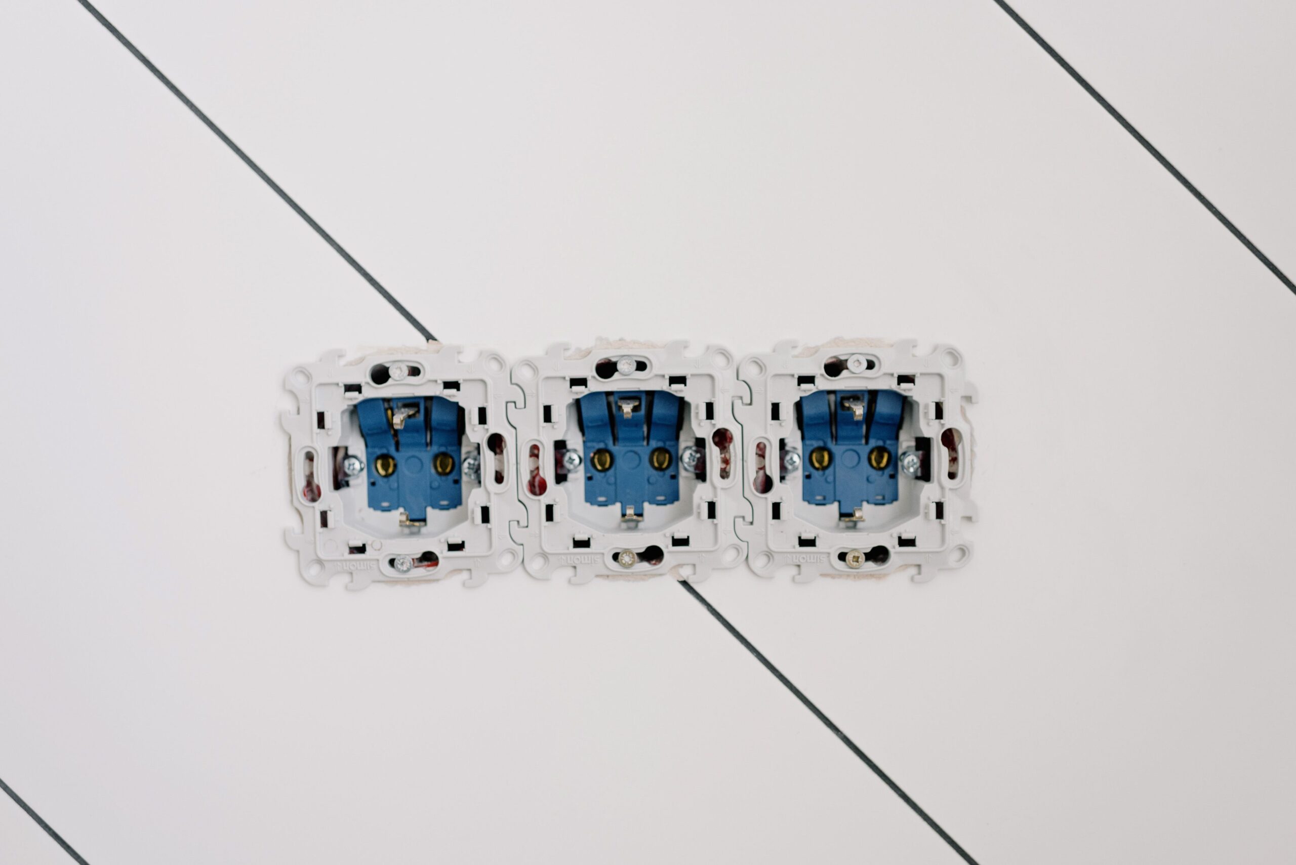 Three white electrical outlet back boxes with blue components mounted on a white wall