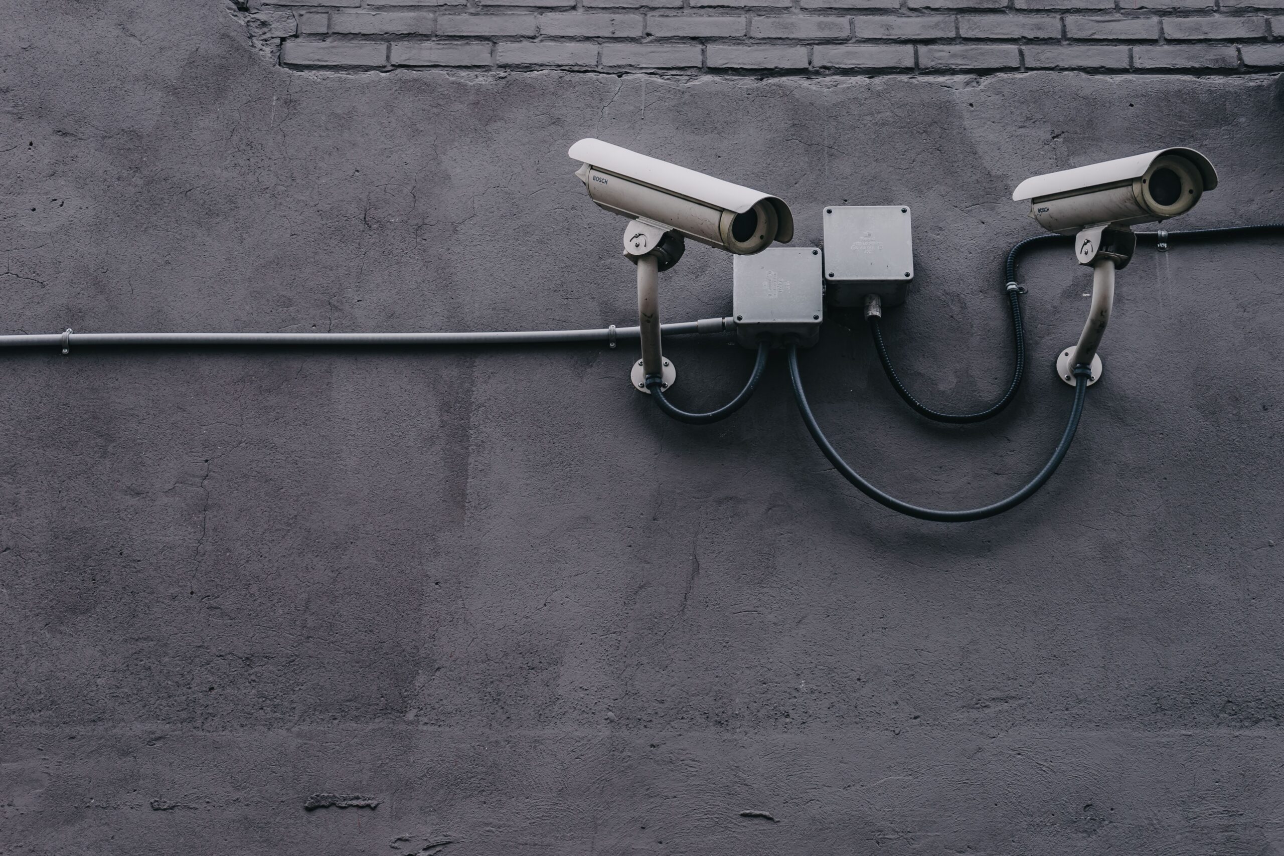 Two white security cameras mounted on a textured gray wall with visible cables outdoor surveillance setup