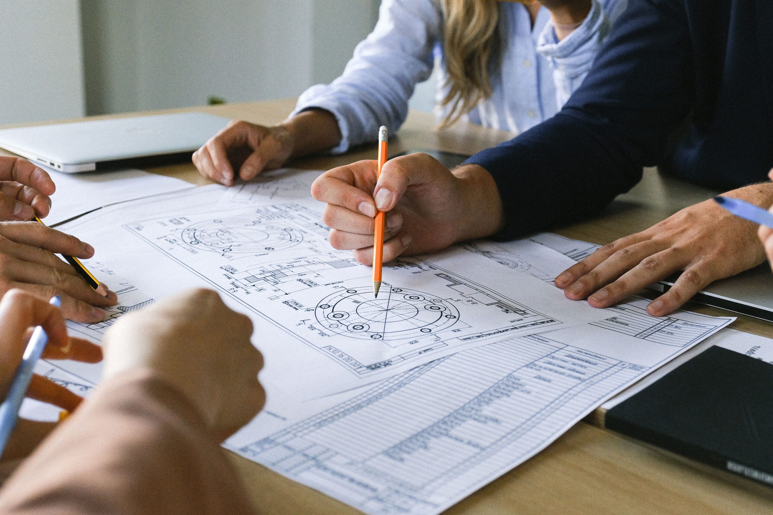 Group of people collaborating on technical blueprints at a table pencils in hand and papers spread out