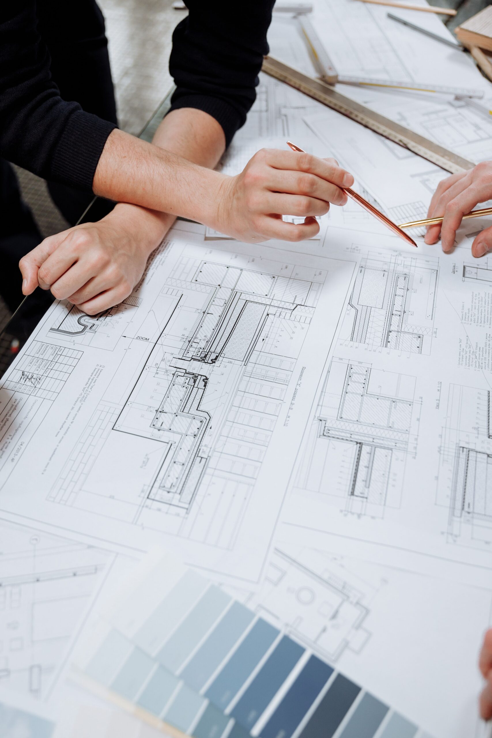 Architects drafting plans on large blueprints with rulers and pencils hands gesturing over detailed architectural drawings on a table