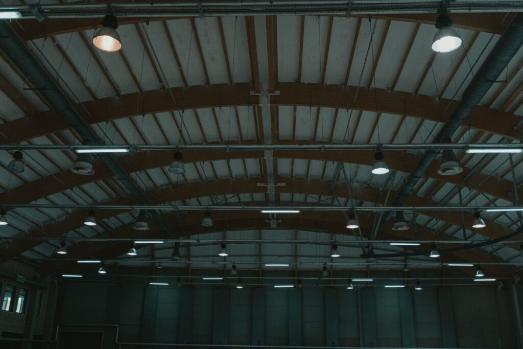 Interior of a large industrial space with exposed wooden roof trusses and numerous hanging lights