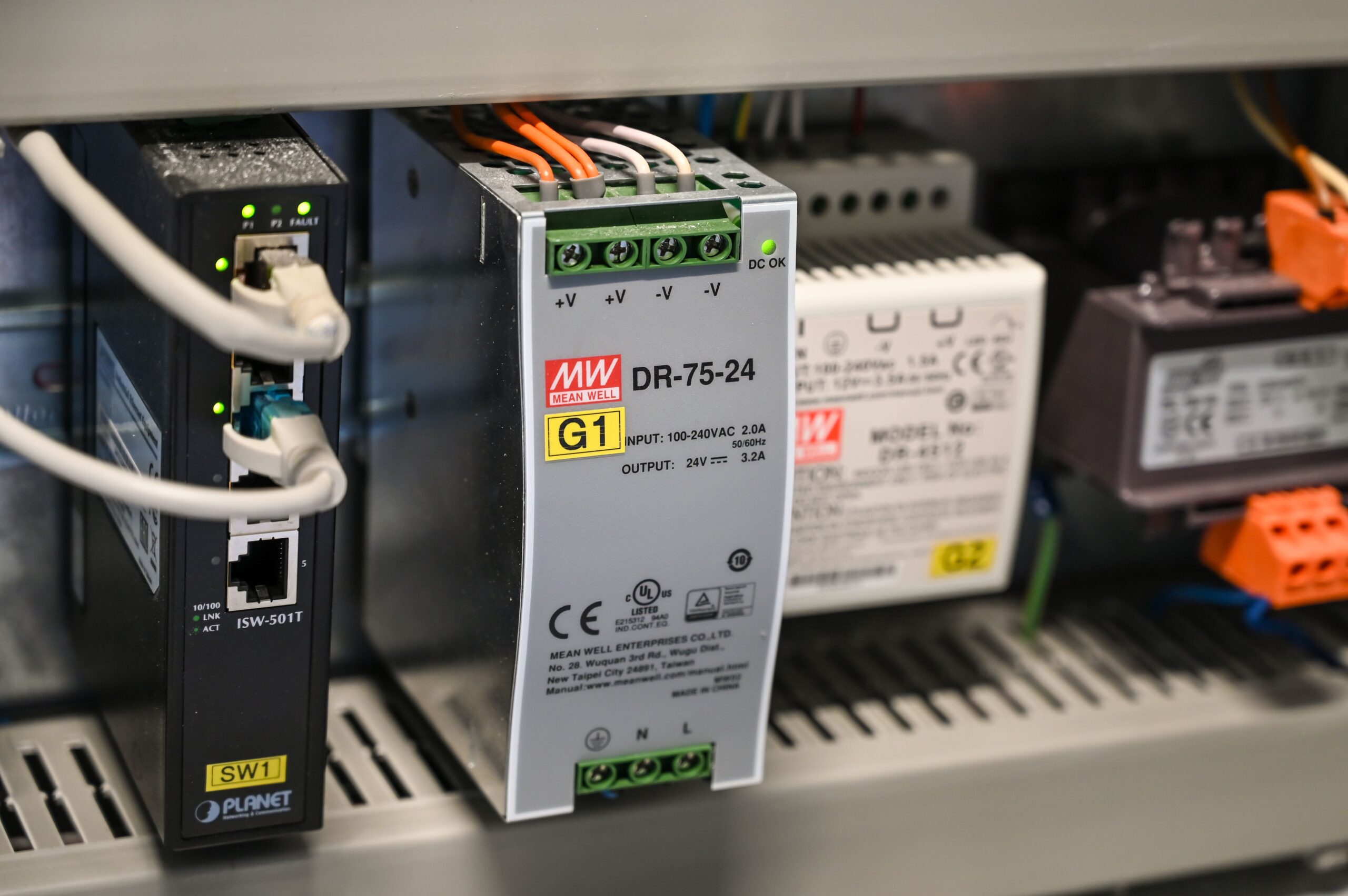 Close up of a Mean Well DR 75 24 power supply in an electrical rack with green terminal blocks and orangewhite wires connected
